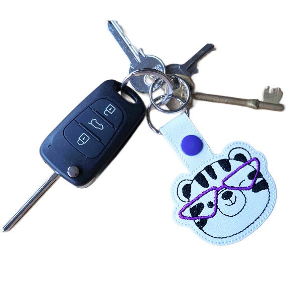 Tiger face keyring with purple glasses attached to a set of keys, showing the keyring in everyday use.