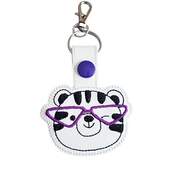 Tiger face keyring with purple glasses, made from white faux leather with a metal split ring and swivel clasp.