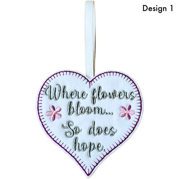 White felt heart hanging decoration with blanket stitch border, embroidered flowers and the message “Where flowers bloom… So does hope”, finished with a white ribbon loop (Design 1)