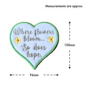 White felt heart hanging decoration with embroidered flowers and the message “Where flowers bloom… So does hope”, shown with approximate measurements of 100mm height and 96mm width