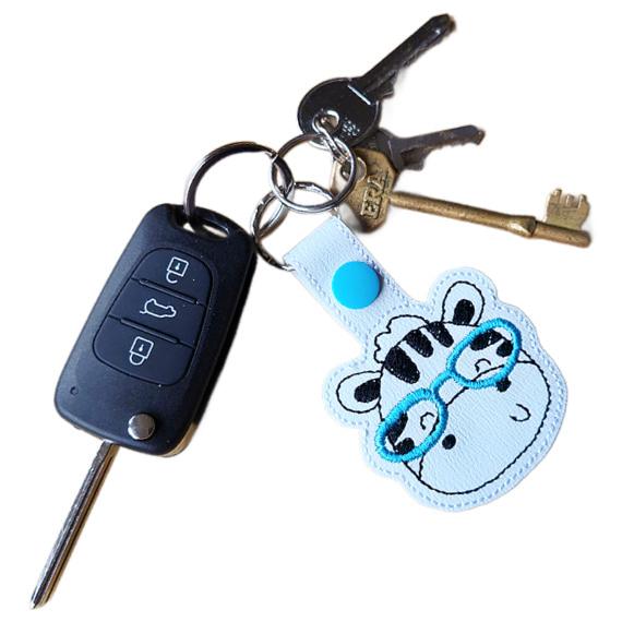 Zebra face keyring with teal glasses attached to a set of keys, showing the keyring in everyday use.