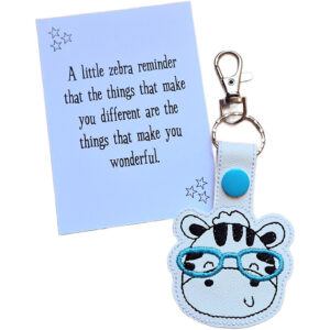 Zebra face keyring with teal glasses shown with matching keepsake card featuring a message about being wonderfully different.