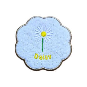 Embroidered April birth flower candle coaster with a white daisy, yellow centre, stitched background detail and a softly scalloped border.