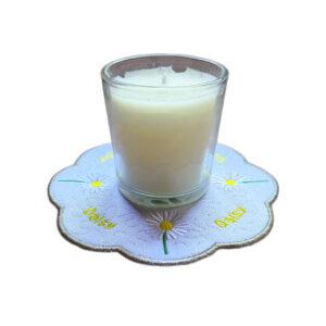 Embroidered April birth flower candle mat with white daisies, yellow centres and a scalloped border, shown underneath a glass candle jar.