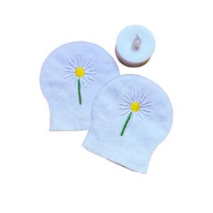 Embroidered April birth flower tealight covers on white felt, with white daisies, yellow centres and green stems, shown beside a battery operated LED tealight.