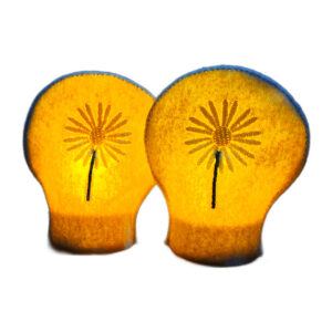 Lit embroidered April birth flower tealight covers on white felt, glowing warmly with daisy designs over battery operated LED tealights.