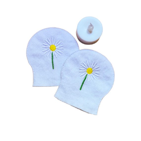 Embroidered April birth flower tealight covers on white felt, with white daisies, yellow centres and green stems, shown beside a battery operated LED tealight.