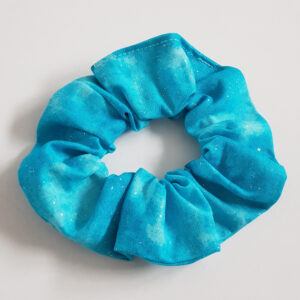 Handmade aqua glitter cotton scrunchie on a plain light background, soft fabric hair tie with subtle sparkle.