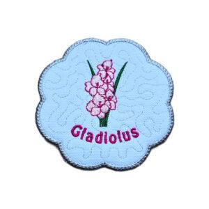 Embroidered August birth flower candle coaster with pink gladiolus blooms, stitched gladiolus text, background detail and a scalloped silver border.
