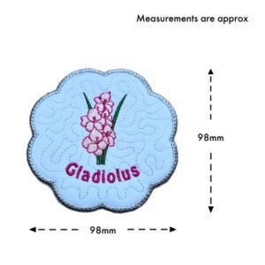 August birth flower candle coaster size guide showing the embroidered gladiolus design with stitched text and scalloped silver border, measuring approximately 98mm x 98mm.