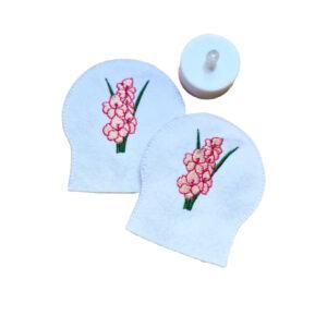 Embroidered August birth flower tealight covers on white felt, with pink gladiolus blooms and green stems, shown beside a battery operated LED tealight.