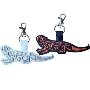 White and black faux leather bearded dragon word art keyrings with embroidered lettering and silver metal lobster clasps.
