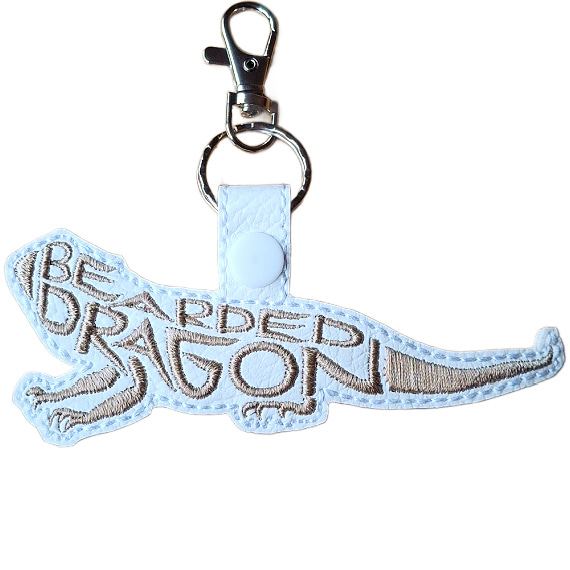 White faux leather bearded dragon word art keyring with silver embroidered lettering and silver metal lobster clasp.