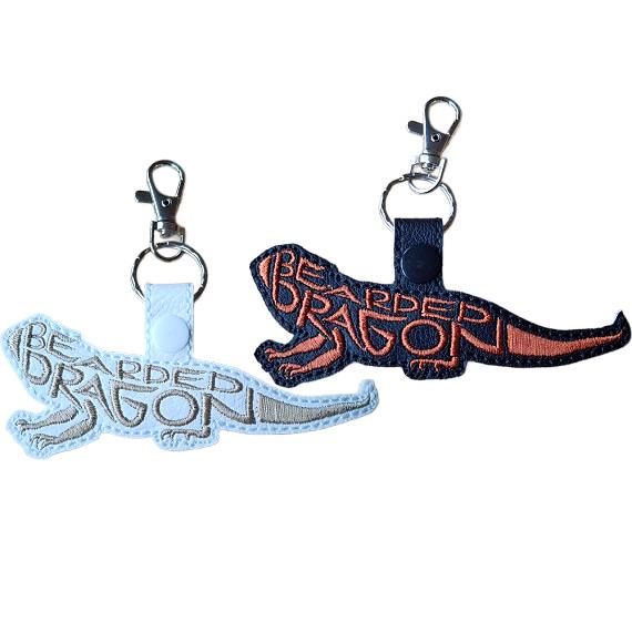 White and black faux leather bearded dragon word art keyrings with embroidered lettering and silver metal lobster clasps.