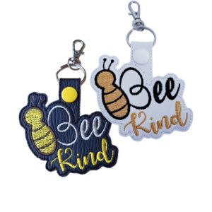 Black and white faux leather Bee Kind keyrings with embroidered bee designs, uplifting wording and silver metal clasps.