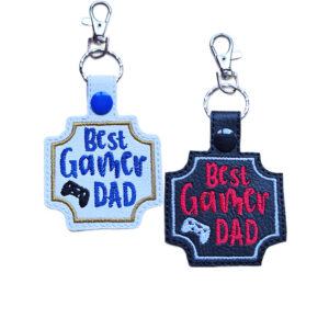 Best Gamer Dad keyrings shown in white and black faux leather, with embroidered gamer lettering, controller detail and sturdy metal keyring hardware.