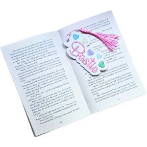 Embroidered 'Bestie' heart bookmark with tassel placed inside an open book, showing how it can be used to mark a reader's page.