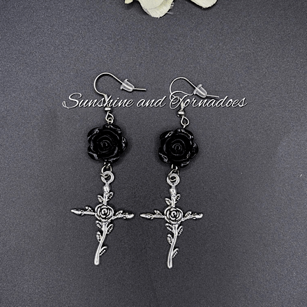 Picture shows a pair of drop earrings featuring a black rose bead and silver cross charms in a gothic style