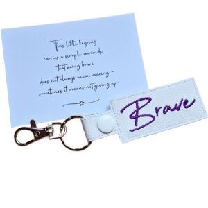 Embroidered Brave keyring in white faux leather, shown beside a matching keepsake card with an encouraging message about bravery.