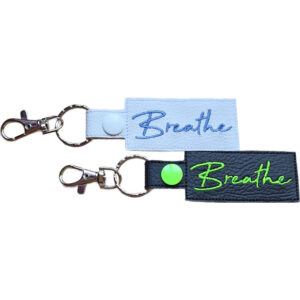 Embroidered Breathe keyring in faux leather, with the word 'Breathe' stitched on black and white backgrounds with sturdy metal hardware.