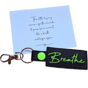 Embroidered Breathe keyring in black faux leather, shown beside a matching keepsake card with a gentle reminder to pause, breathe and begin again.