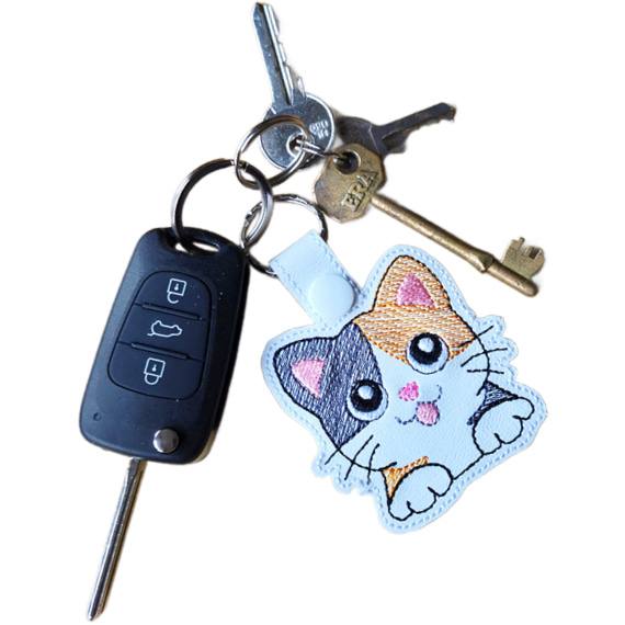 White faux leather calico cat keyring attached to a set of keys, showing its size and everyday use.