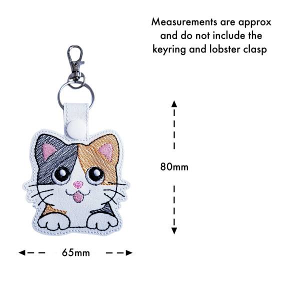 White faux leather calico cat keyring with size guide showing approximate measurements of 80mm x 65mm, excluding the keyring and lobster clasp.