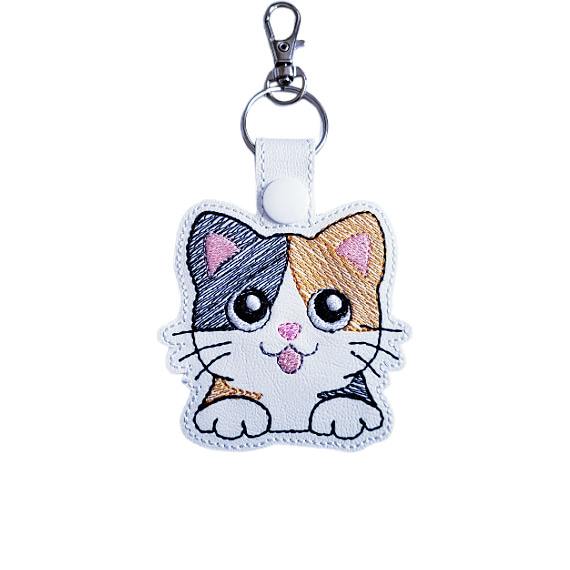 White faux leather calico cat keyring with embroidered kawaii cat design, big eyes, and silver metal clasp.