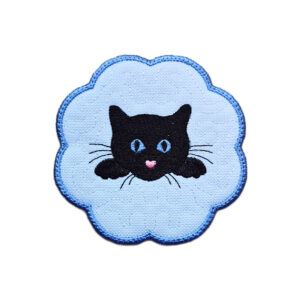 Embroidered cat candle coaster with a black cat peeking over the edge, bright stitched details and a scalloped blue border.