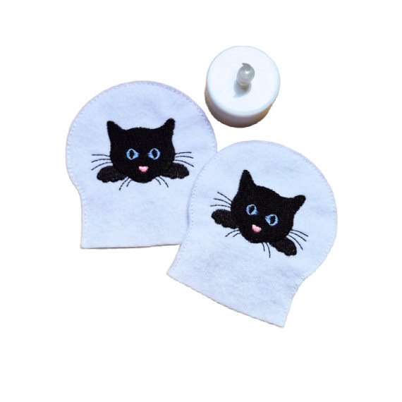 Embroidered cat LED tealight covers on white felt, with black cat faces and bright stitched details, shown beside a battery operated tealight.
