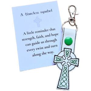 White faux leather Celtic Cross keyring with green embroidered details, shown with a matching keepsake card about strength, faith and hope.