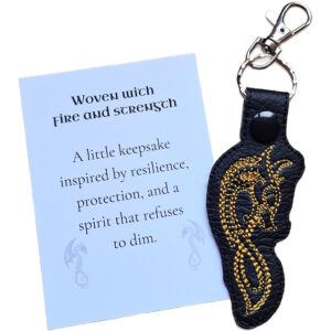 Black Celtic Dragon keyring with gold embroidered dragon design, shown with a matching keepsake card about fire, strength and resilience.