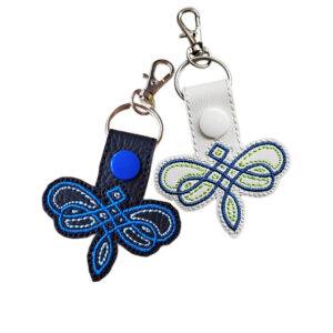 Black and white Celtic Dragonfly keyrings with embroidered knotwork-style designs, coloured snaps and silver metal clasps.