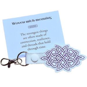 White Celtic Knot keyring with purple embroidered knotwork design, shown with a matching keepsake card about connection, resilience and meaning.