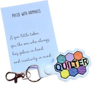 White faux leather quilter keyring with a colourful patchwork-style design, shown with a keepsake card reading 'Pieced with Happiness'.