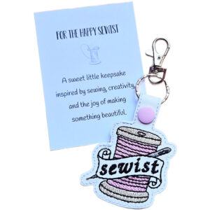 White faux leather Sewist keyring with a pink thread spool and needle design, shown with a keepsake card reading 'For the Happy Sewist'.