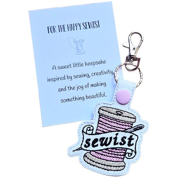 White faux leather Sewist keyring with a pink thread spool and needle design, shown with a keepsake card reading 'For the Happy Sewist'.
