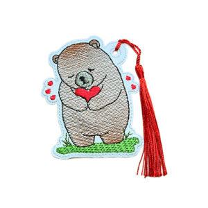 Embroidered bear bookmark holding a heart with small heart details, pale blue edging and coordinating tassel, designed as a cute reading gift.