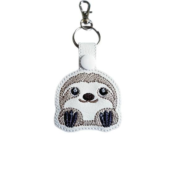 White faux leather cute sloth keyring with an embroidered kawaii sloth face, white snap fastening and silver lobster clasp hardware.