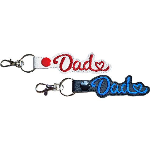 Dad Heart keyrings shown in white and black faux leather, with embroidered Dad lettering, heart detail and sturdy metal keyring hardware.