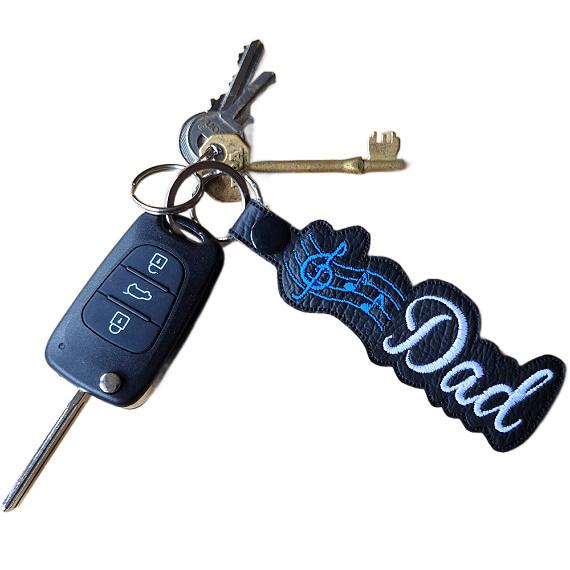 Embroidered Dad Music Note keyring in black faux leather with blue musical notes and white Dad lettering, attached to a set of keys.