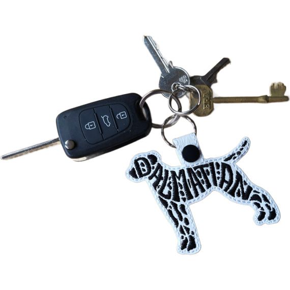White embroidered Dalmatian word art keyring attached to a set of keys, showing its size and everyday use.
