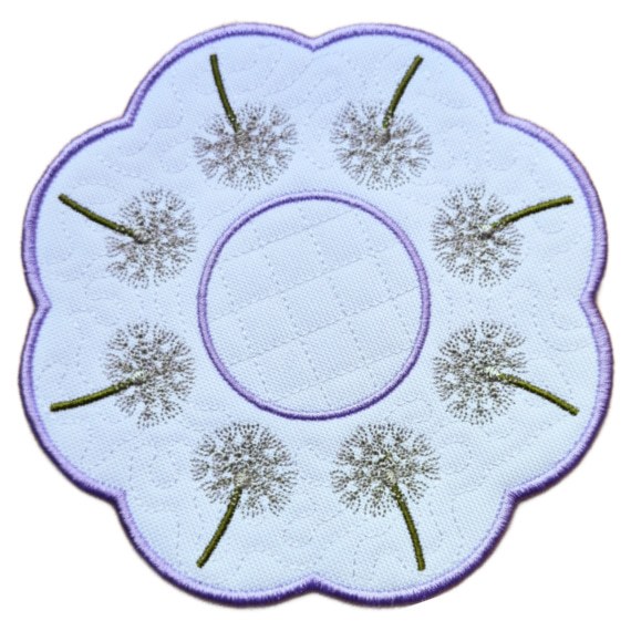 Close up of an embroidered dandelion seed head candle mat with a scalloped purple border, circular centre and delicate dandelion clocks stitched around the edge.