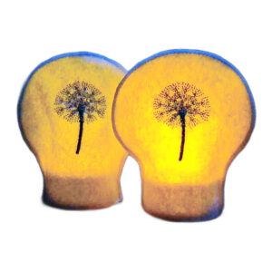 Two lit dandelion seed head tealight covers glowing warmly over LED tealights, with embroidered dandelion clocks on white felt.