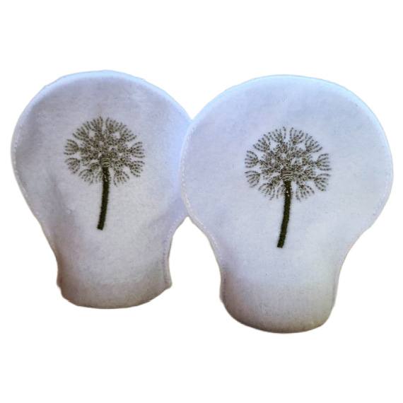 Two unlit dandelion seed head tealight covers made from white felt, each embroidered with a delicate dandelion clock design.