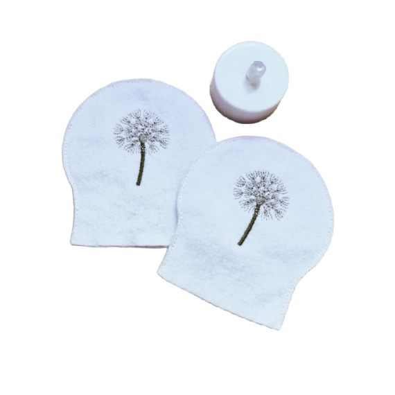 Two embroidered dandelion seed head tealight covers made from white felt, shown with an LED tealight for display.