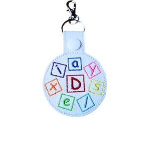 Colourful embroidered Dyslexia Awareness keyring made from white faux leather, featuring bright stitched letter blocks and silver metal keyring hardware.