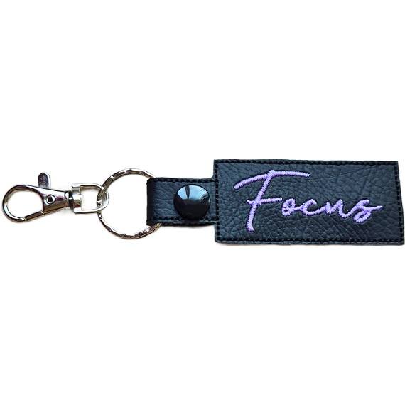 Embroidered Focus keyring in black faux leather, with the word 'Focus' stitched in lilac and sturdy metal keyring hardware.