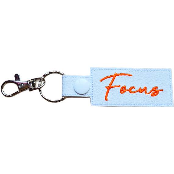 Embroidered Focus keyring in white faux leather, with the word 'Focus' stitched in orange and sturdy metal keyring hardware.