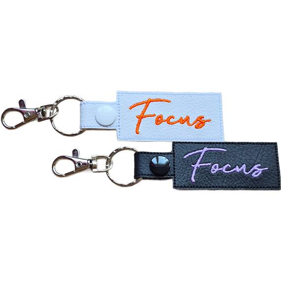 Embroidered Focus keyring in faux leather, with the word 'Focus' stitched on black and white backgrounds with sturdy metal hardware.